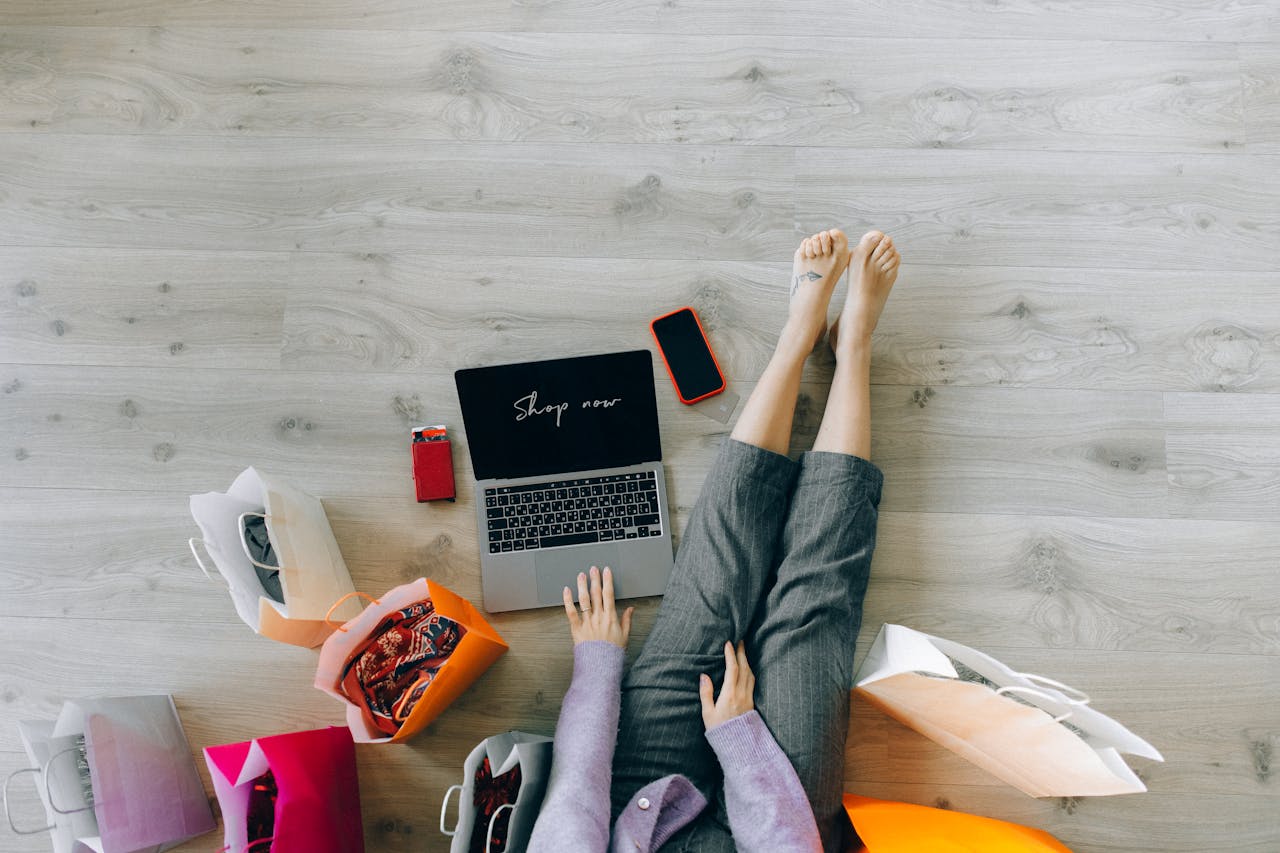 Woman shopping online with laptop and paper bags from above view.